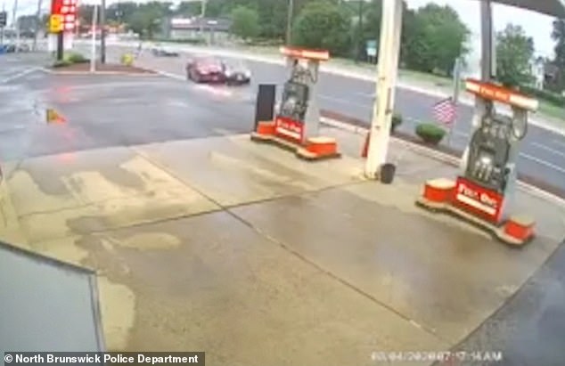 A grey car begins to turn into the gas station when a red car in the same lane crashes into it and throws it off course